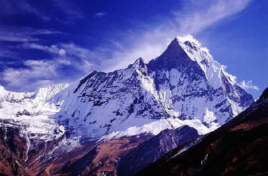 A majestic view of the snow-capped Machapuchare mountain peak in the Himalayas under a blue sky with scattered clouds.