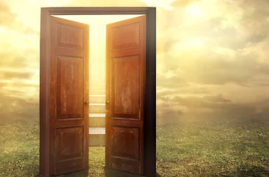A large dark wooden double door standing wide open in the middle of a grassy field, revealing steps of a staircase bathed in bright golden sunlight shining through clouds, symbolizing renewal in Adyar.