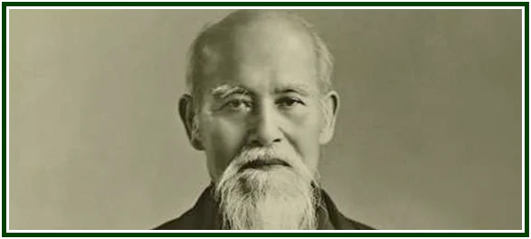 Historical portrait of Morihei Ueshiba, the founder whose teachings established the philosophy of aikido, showing his serene face with a long white beard and mustache against a neutral studio background.