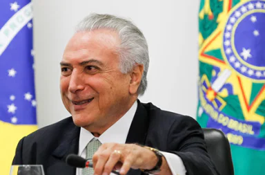 Michel Temer smiling in front of the flags of Brazil, representing the diplomatic stance on Brazil and nuclear proliferation.