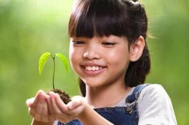 A young girl smiling while holding a small growing plant, symbolizing the moral causes and karma that shape the world state.